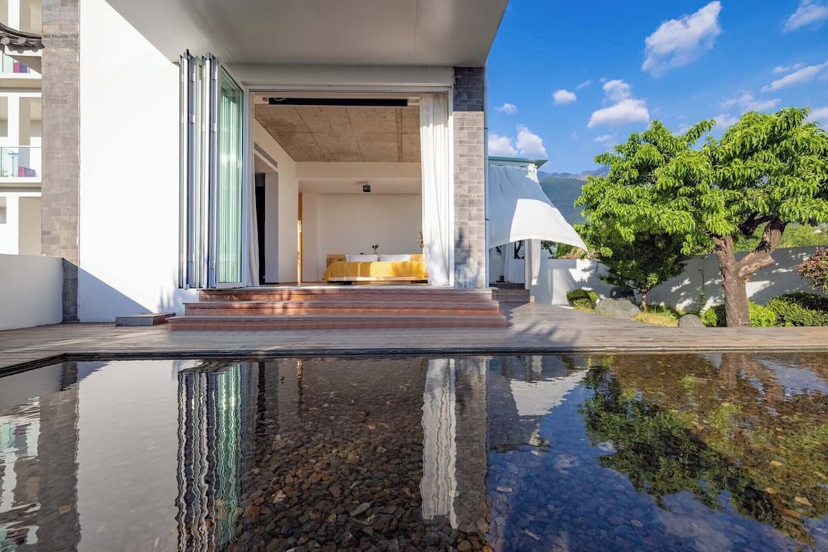 A modern hotel with a pool, a bed with a yellow cover, and a tree in the background.