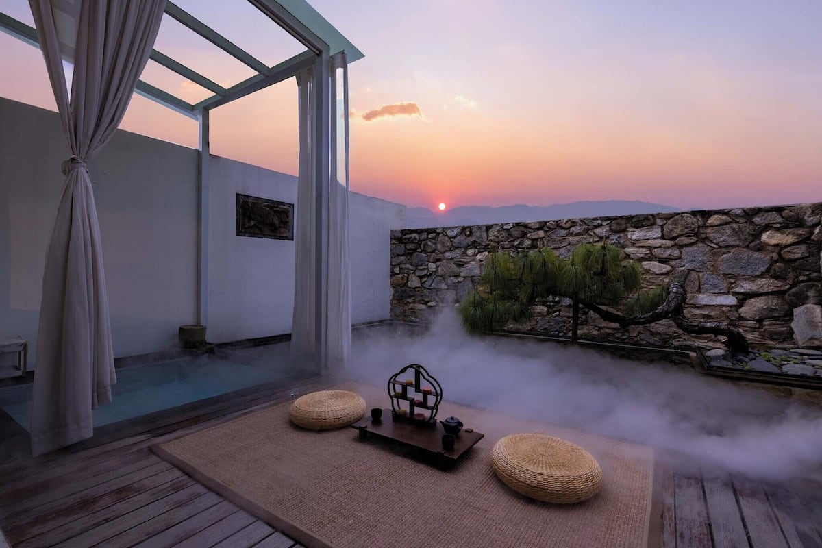 A serene indoor setting with a stone wall, a wooden deck, and a view of the sunset.