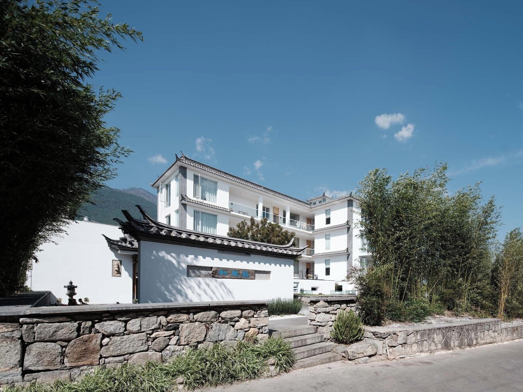 A traditional multi-story building with a white facade, a stone wall in the foreground, and a clear blue sky.