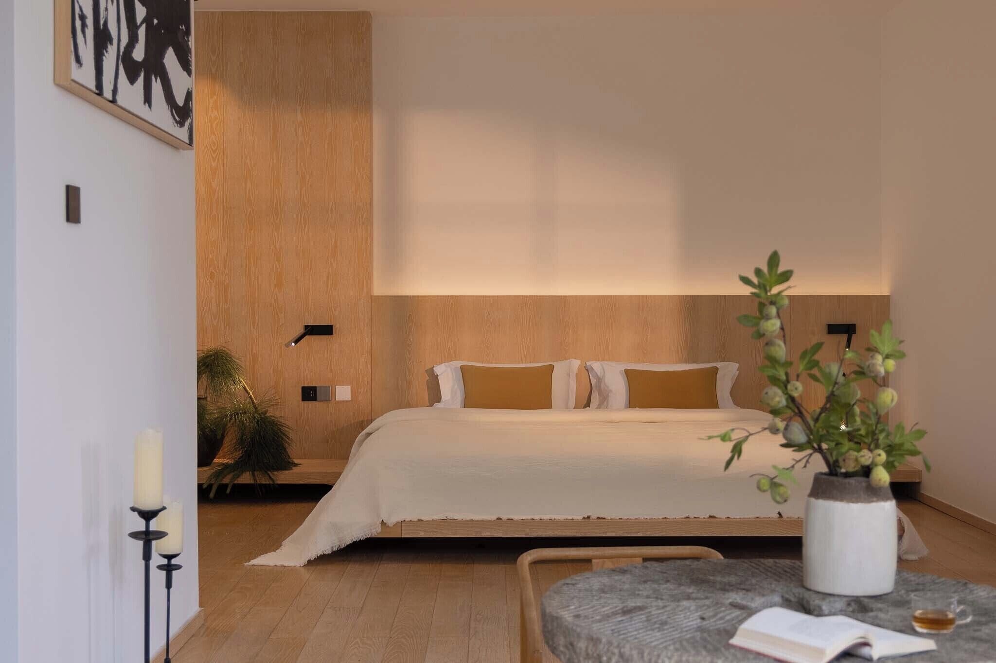 Un dormitorio con cama, mesita de noche, lámpara y planta en maceta.