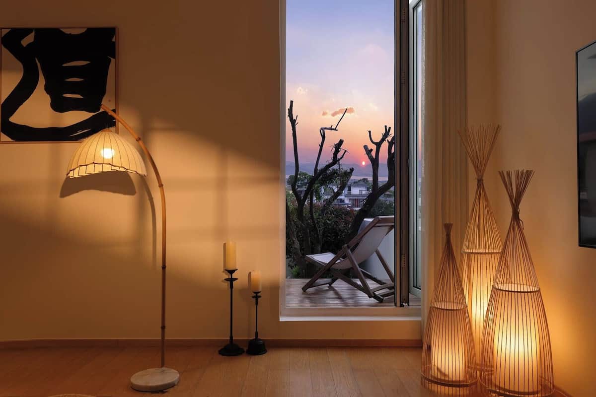 A room with a large window, a floor lamp, a chair, and decorative candle holders.