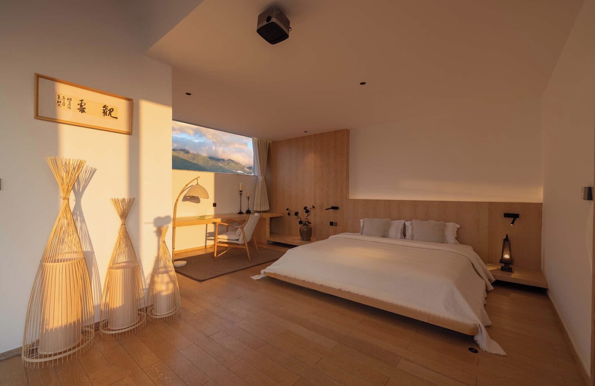 A modern bedroom with a large bed, a desk, and a view of mountains.