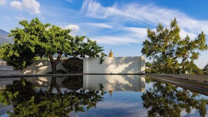 Un espace extérieur paisible, avec une étendue d’eau qui reflète la lumière, des arbres et, au loin, une structure ressemblant à une pagode.