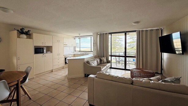 A compact living space with a kitchenette, a sofa, a dining table, and a TV. - Allamanda Place Unit 11 Bulcock Beach Waterfront Views (Caloundra)