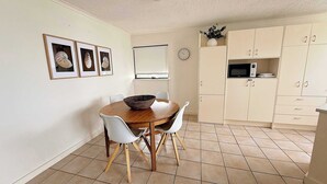 A dining area with a round wooden table, white chairs, and a white ceiling. - Allamanda Place Unit 11 Bulcock Beach Waterfront Views (Caloundra)