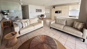A living room with two sofas, a dining table, and a kitchen area. - Allamanda Place Unit 11 Bulcock Beach Waterfront Views (Caloundra)