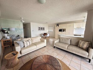 A living room with two sofas, a dining table, and a kitchen area. - Allamanda Place Unit 11 Bulcock Beach Waterfront Views (Caloundra)