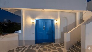 Una puerta azul con dos luces, piso de piedra y pared blanca.