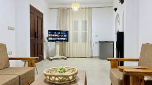 Una sala de estar con un televisor de pantalla plana, un refrigerador pequeño y un banco de madera.