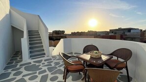 Una terraza en la azotea con mesa y sillas, una escalera y vistas de edificios al fondo.