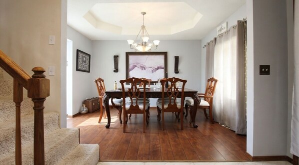 Un espace repas avec une table et des chaises en bois, un lustre et un escalier.