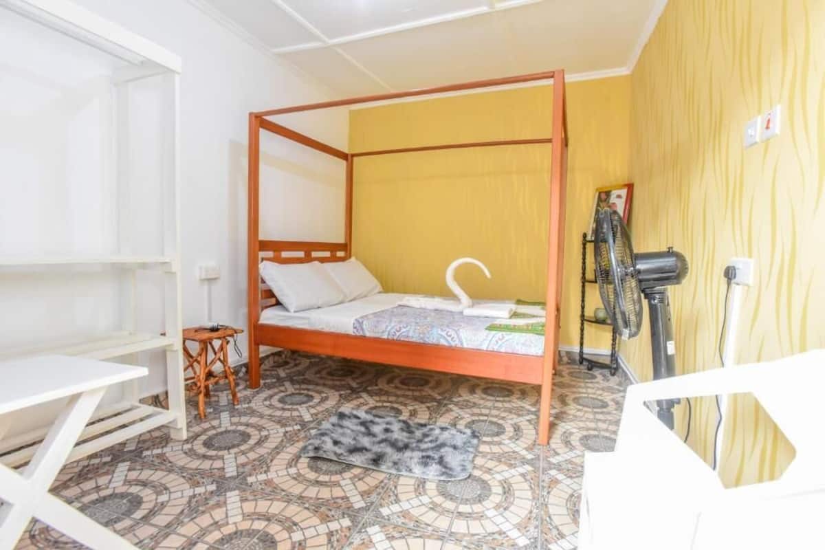 Una habitación con una cama con dosel, una mesita, una silla, un ventilador y un suelo estampado.