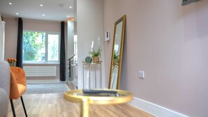 Un interior moderno con suelo de madera, una mesa redonda de vidrio, un espejo grande y vistas a un área exterior a través de un ventanal.