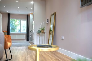 Ein modernes Interieur mit Holzboden, einem runden Glastisch, einem großen Spiegel und Blick durch eine Glastür in einen Außenbereich.