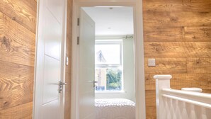 Una habitación con paredes de madera, una puerta blanca, una ventana con vistas y una barandilla blanca.