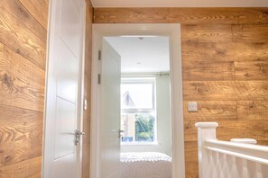 Ein Zimmer mit Holzwänden, einer weißen Tür, einem Fenster mit Blick und einem weißen Geländer.