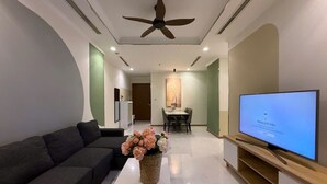 Ein modernes Wohnzimmer mit einer Couch, einem Flachbildfernseher, einem Deckenventilator und einem Essbereich im Hintergrund.
