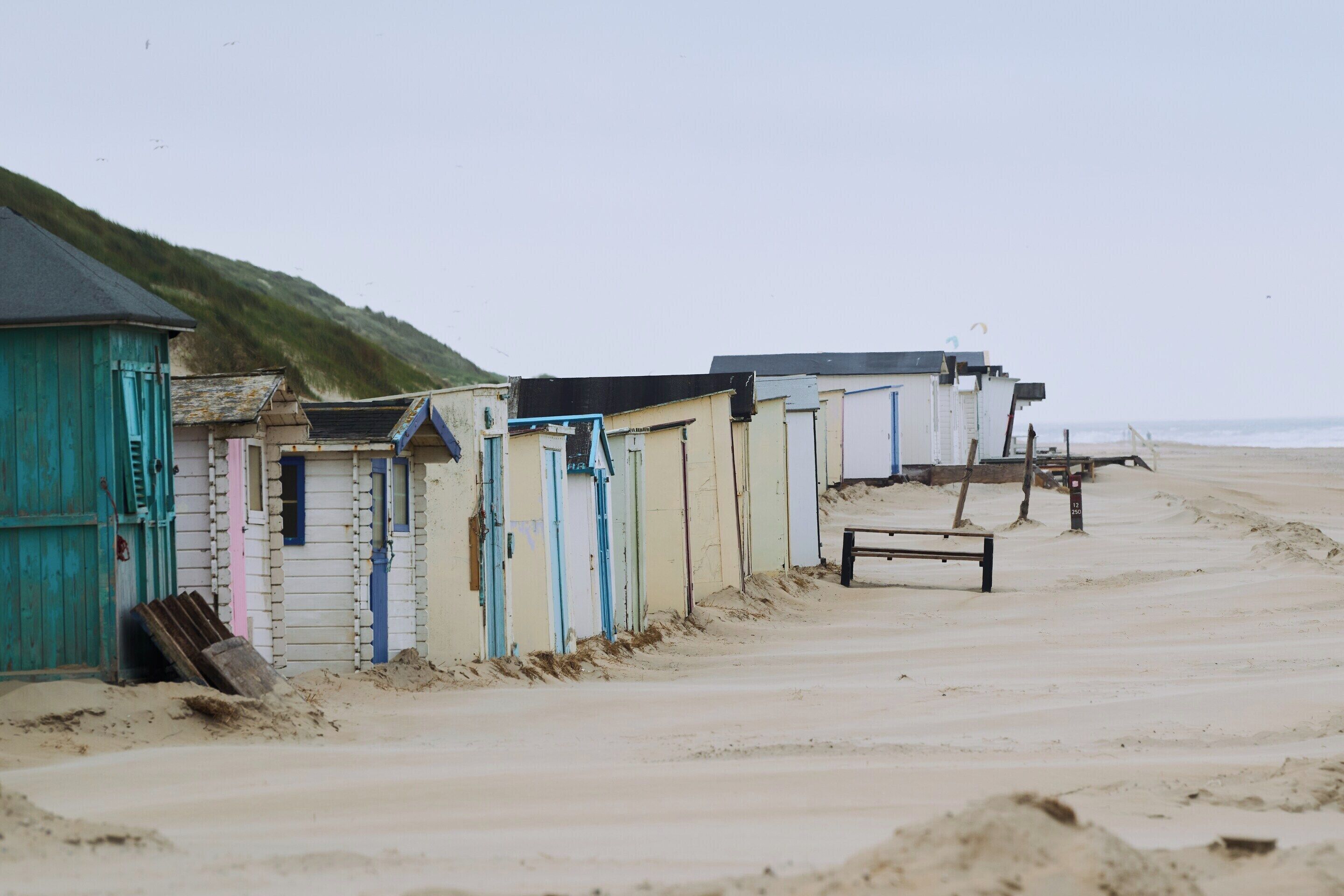 A row of beach huts with a sandy beach and ocean in the background.