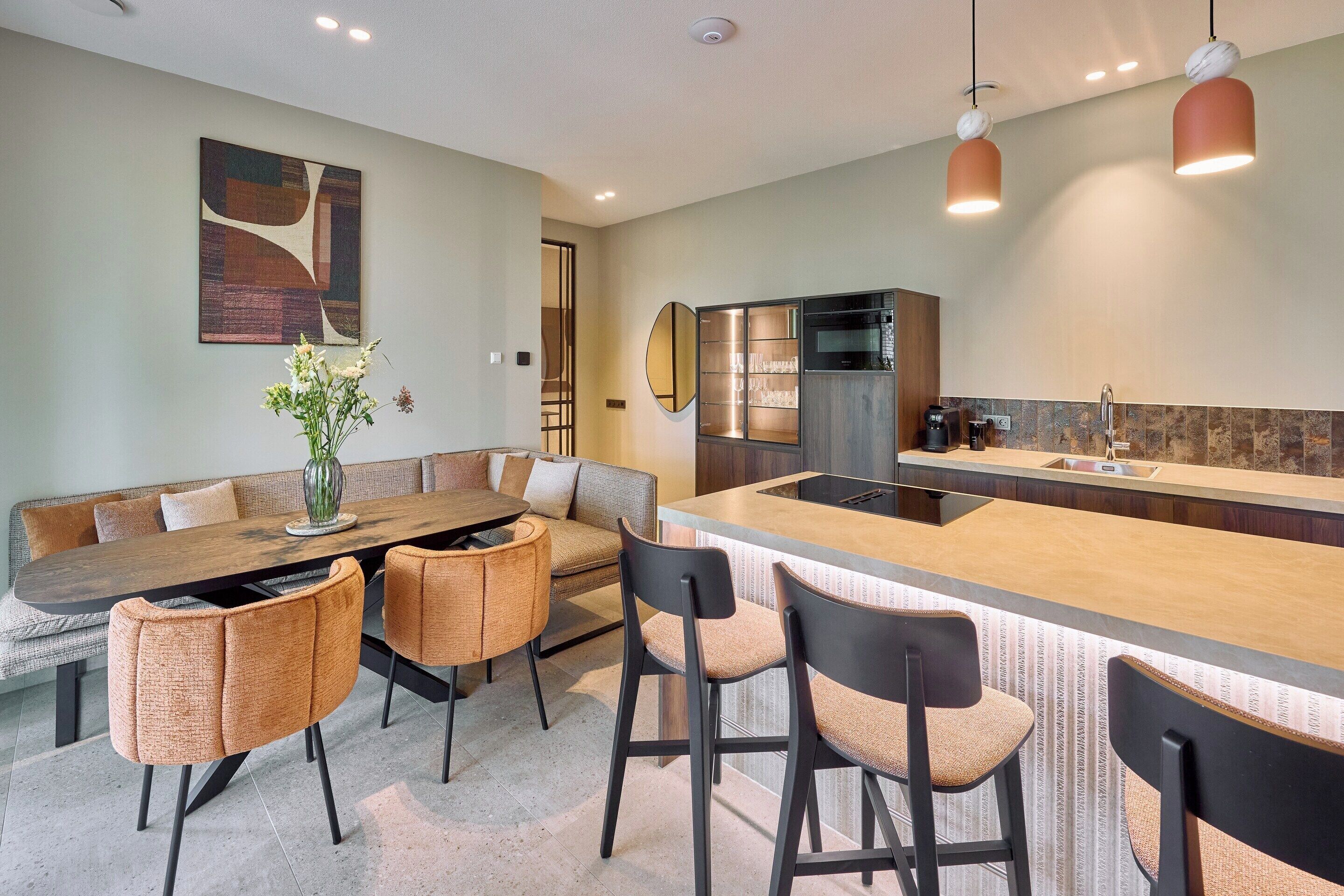 A modern kitchen with a central island, bar stools, a dining table with cushioned chairs, and a large abstract painting on the wall.