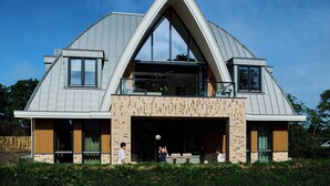 Una casa moderna con techo triangular, ventanas grandes y garaje cubierto.