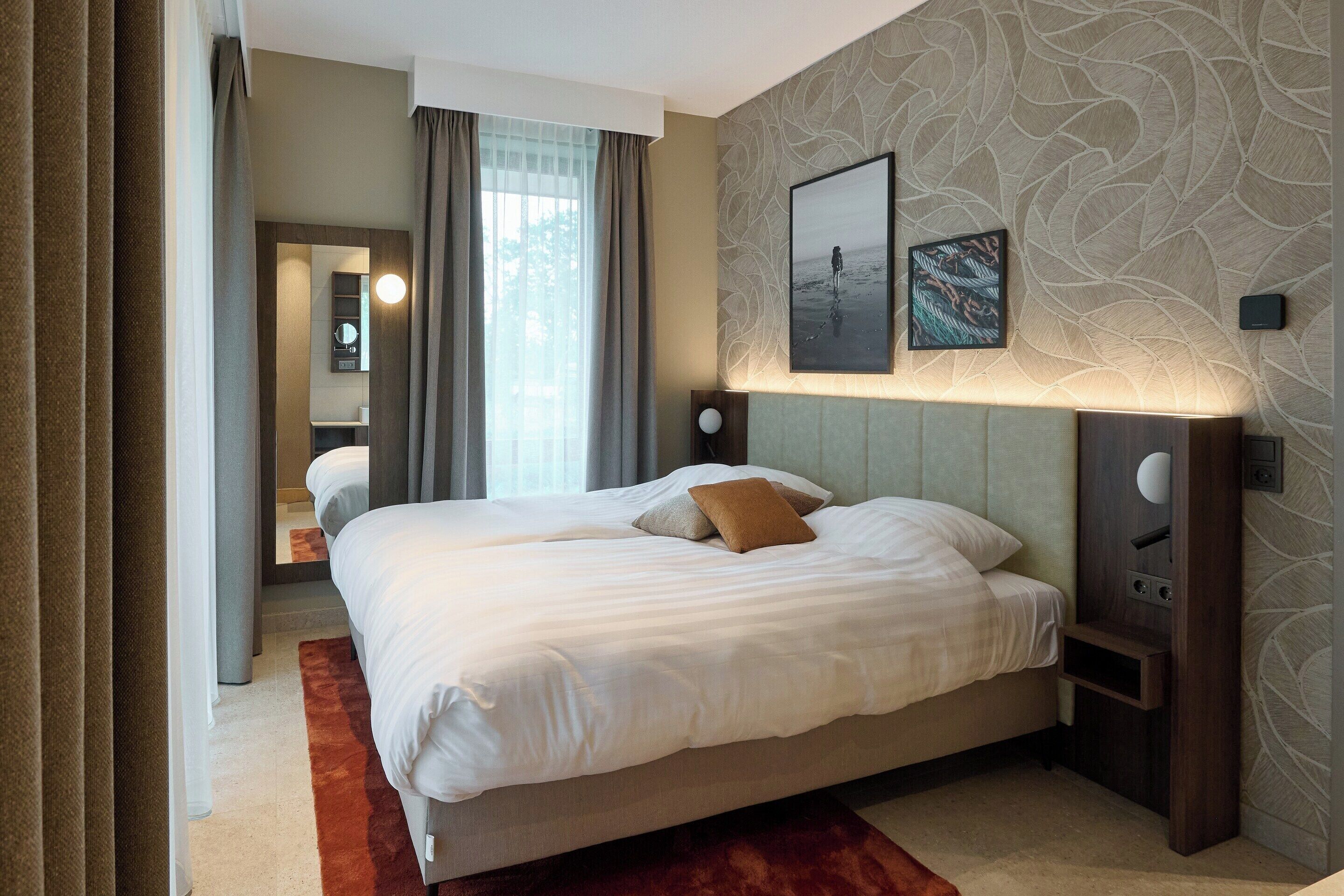 A hotel room with a large bed, a mirror, a wall-mounted picture, and a nightstand.