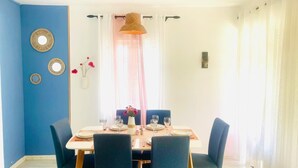 Comedor con una mesa preparada para cuatro, paredes azules y una ventana con cortinas traslúcidas.