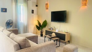 Una sala de estar moderna con un conjunto de sofás, un televisor montado en la pared, una mesita de noche con una lámpara y una planta en maceta.