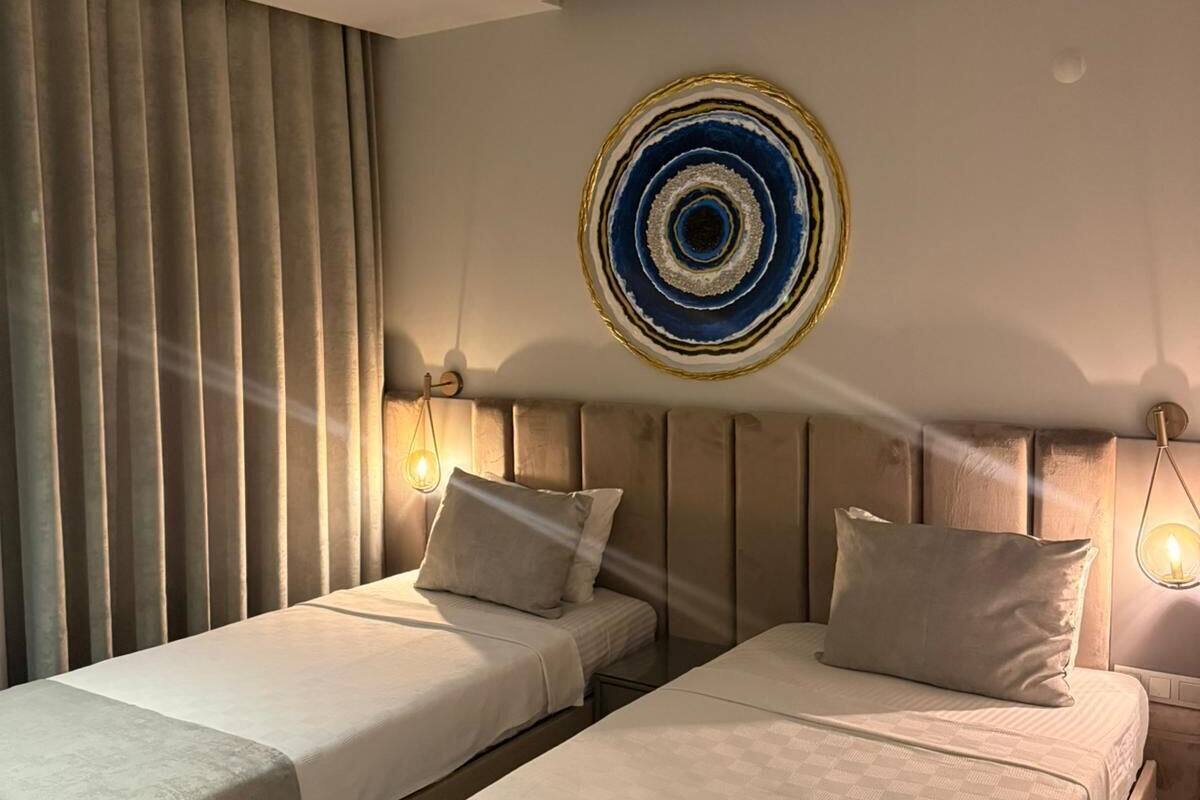 A hotel room with two beds, a large circular artwork on the wall, and a window with curtains.