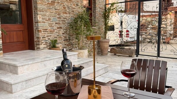 A stone building with a wooden door, a table with wine glasses and a bottle, and a chair. - The Pilgrim Ephesus Hotel (Selcuk)