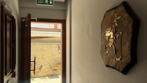 A hallway with a wooden door, a wall-mounted sign indicating an exit, and a rustic wall decoration. - The Pilgrim Ephesus Hotel (Selcuk)