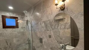A bathroom with a marble sink, a mirror, a shower, and a wall-mounted light fixture. - The Pilgrim Ephesus Hotel (Selcuk)