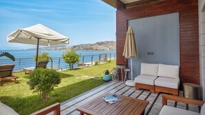 Um terraço com vista para o mar, uma mesa de madeira, um sofá e um guarda-sol.