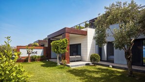Uma casa moderna com dois andares, gramado bem cuidado, uma pequena árvore e uma placa com a inscrição 'Boot'.