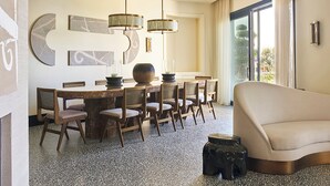 Quarto de hotel moderno com área de refeições, sofá e uma janela grande.
