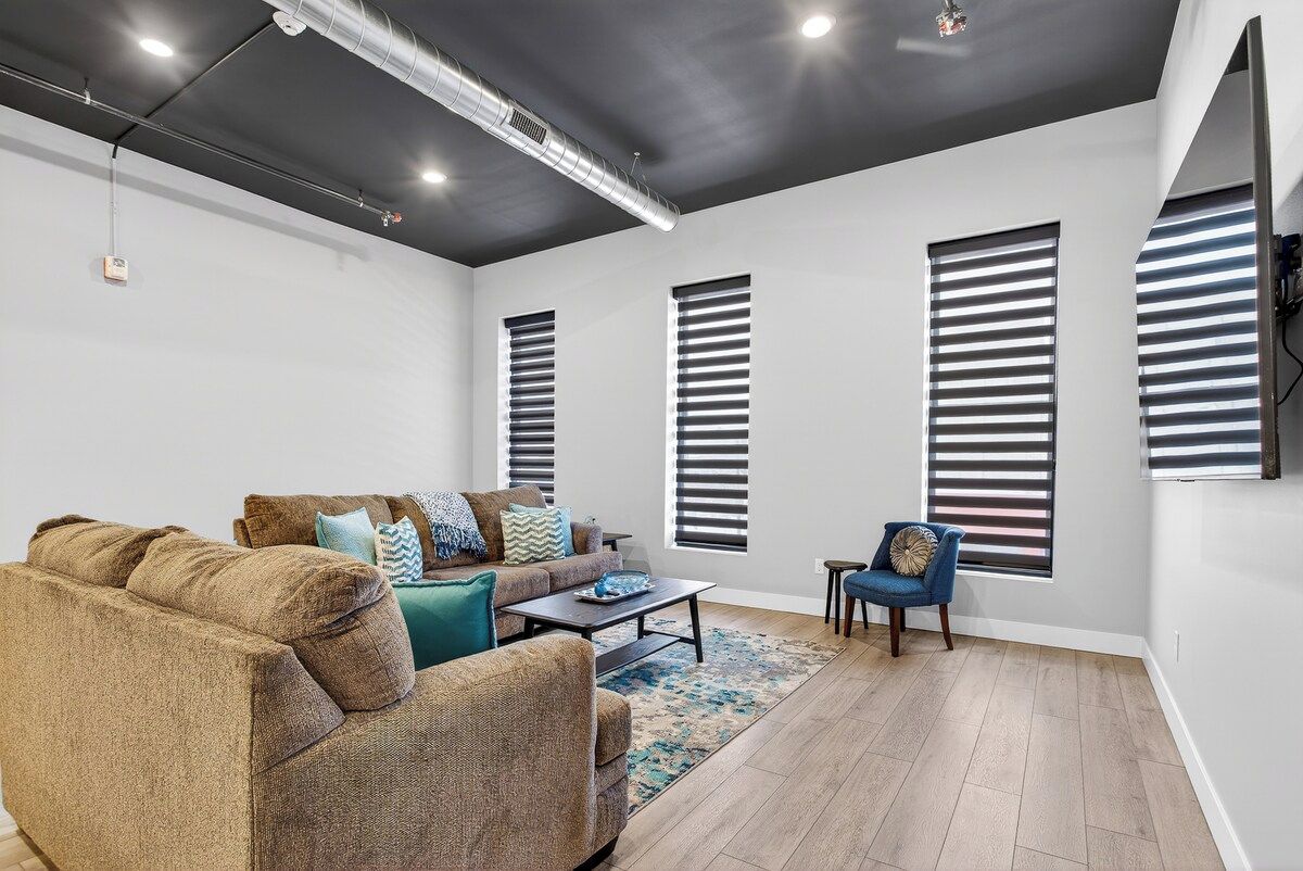 Una sala de estar moderna con un sofá, una mesa de centro y una silla. Hay tres ventanas con persianas.