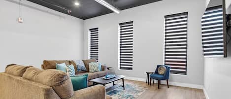 Una sala de estar moderna con un sofá, una mesa de centro y una silla. Hay tres ventanas con persianas.