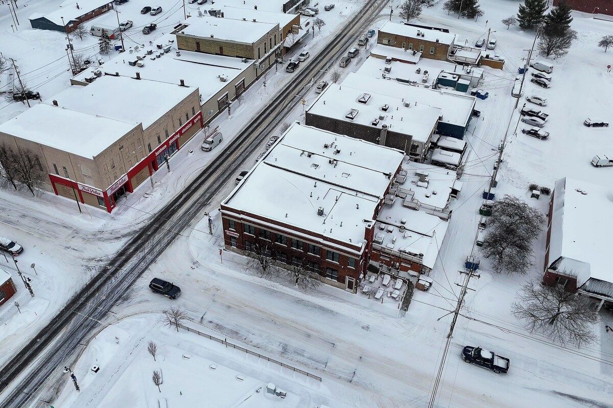 Vista aérea de una zona comercial con varios edificios, estacionamientos y calles cubiertas de nieve.