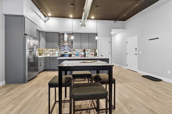 A modern kitchen with a central island, bar stools, and stainless steel appliances. - The Lofts - Unit 3 (Fennville)
