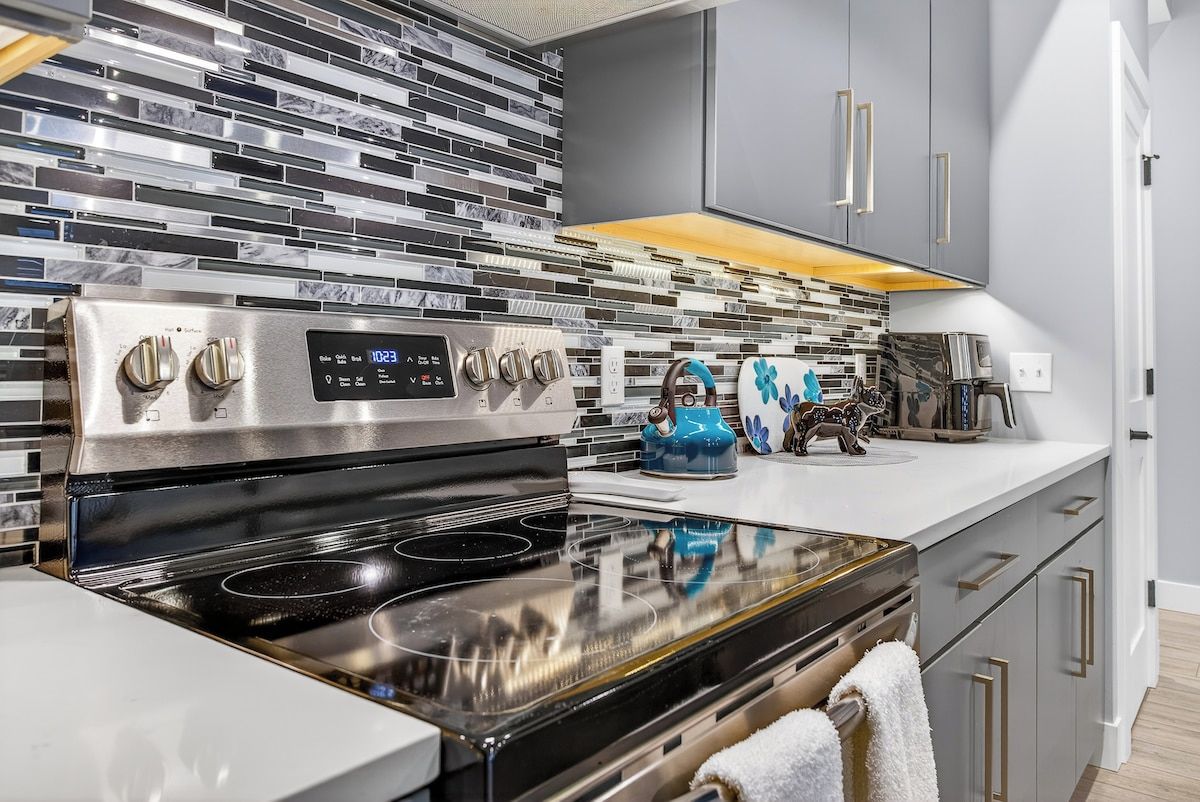 A modern kitchen with a stainless steel stove, a digital clock, and a patterned backsplash.