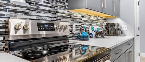 A modern kitchen with a stainless steel stove, a digital clock, and a patterned backsplash.