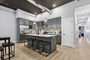 A modern kitchen with a central island, bar stools, stainless steel appliances, and pendant lighting.