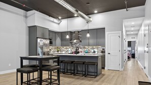 Et moderne køkken med en central ø, barstole og et rustfrit stålkøleskab.