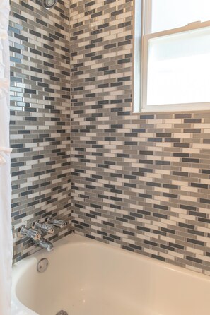 A corner of a bathroom with a white bathtub, a tiled wall, and a window.