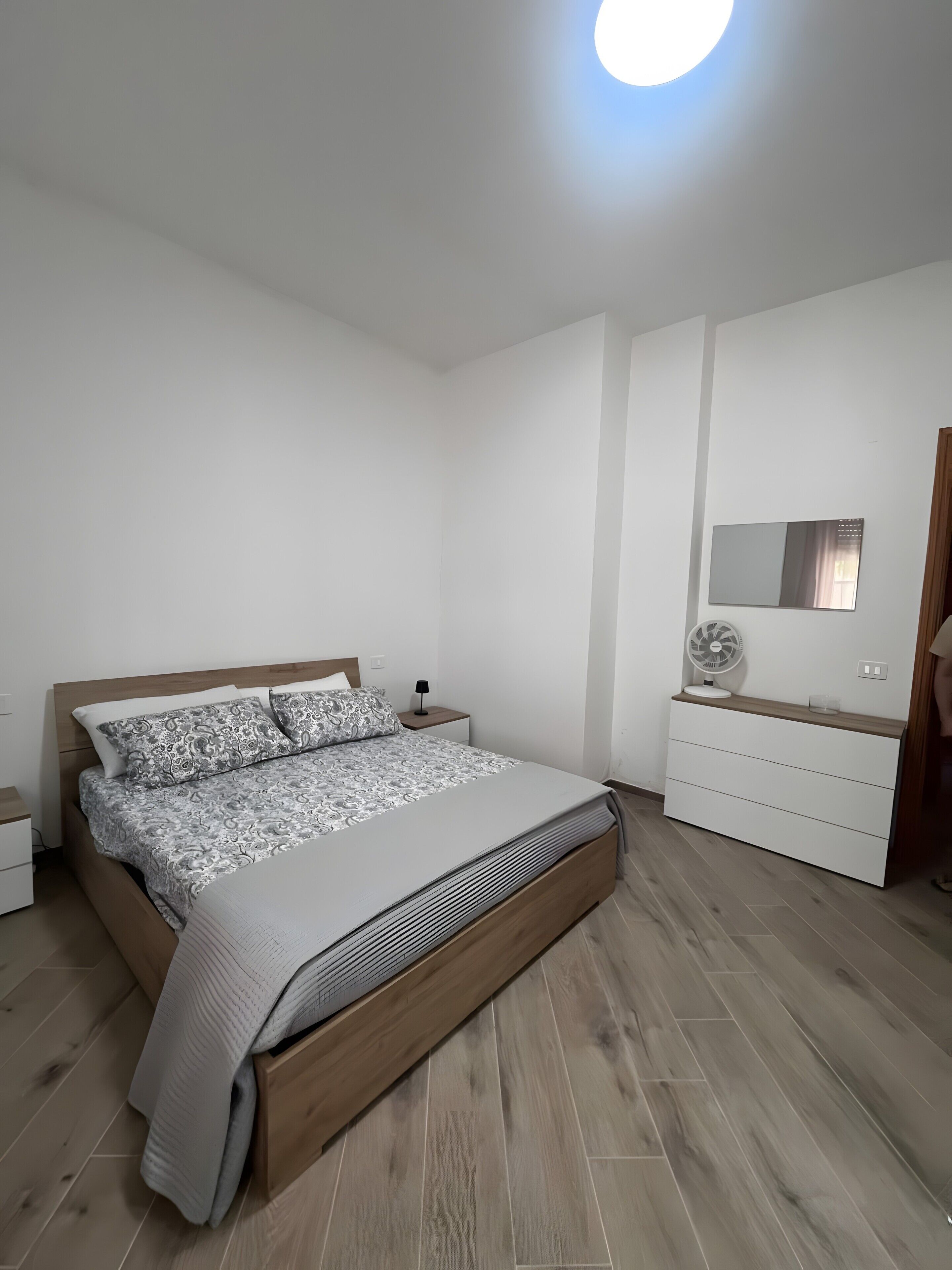 Una camera da letto con un letto, comodini, una cassettiera, uno specchio e una luce a soffitto.