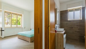 Een slaapkamer met een houten bed, een raam en een badkamer met een houten wastafel.
