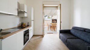 Een moderne keuken met een houten aanrecht, een ingebouwde oven en witte kastjes. Door een open deur is een eethoek met een tafel en stoelen zichtbaar.