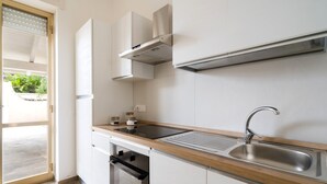 Ett modernt kök med en inbyggd ugn, en diskho i rostfritt stål och ett fönster med persienner.