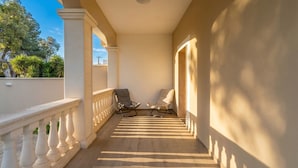 En täckt utomhuskorridor med två stolar, en balustrad och utsikt över träd och himmel.