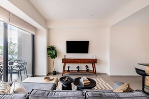 Ein modernes Wohnzimmer mit einer Couch, einem Couchtisch, einem an der Wand montierten Fernseher und einem Essbereich mit Stühlen und einem Tisch.