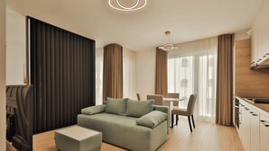 A modern living room with a sofa, ottoman, dining table, and kitchen area. - Nest Inn Jasmine Apartment (Oradea)